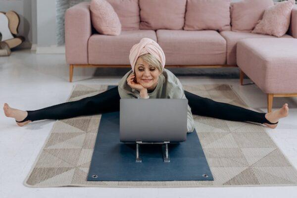 An older woman doing splits while researching healthy living in your golden years on her laptop