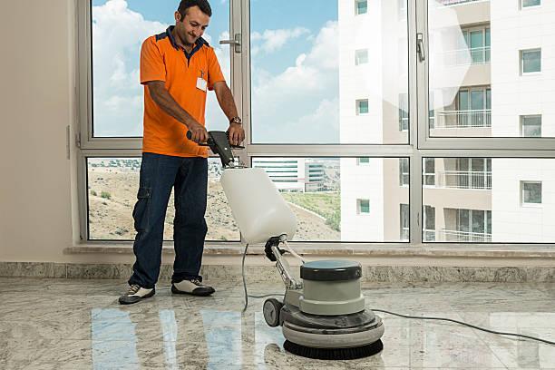 Worker wearing uniform cleaning marble floor with buffer machine.
